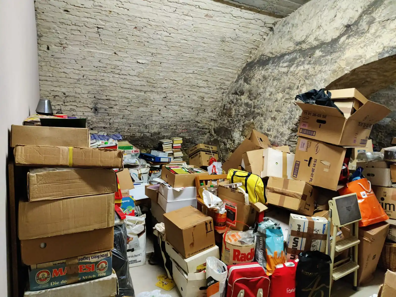 Pakete und Bücher, Leitern, Taschen und sonstige Gegenstände, die im Lagerraum regelmäßig und ungeordnet übereinander gestapelt sind